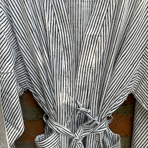 May include: A black and white striped robe with a matching belt. The robe has long sleeves and pockets. The vertical stripes are evenly spaced. The robe is made of a lightweight fabric.