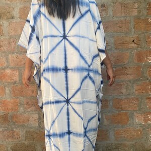 May include: A white caftan dress with a blue geometric tie-dye pattern. The dress has wide sleeves and a loose, flowing fit. The fabric appears lightweight. The dress is knee-length.