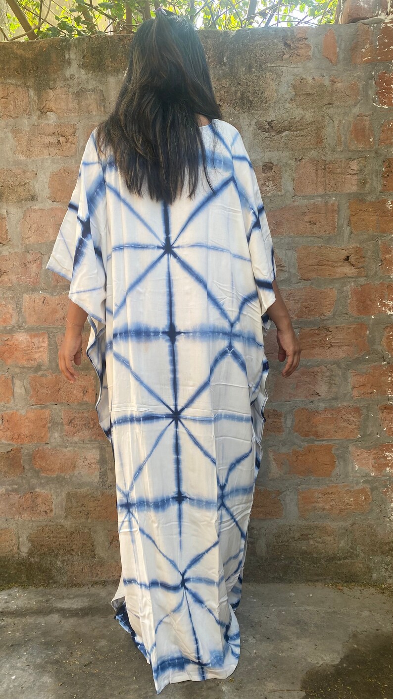 May include: A white caftan dress with a blue geometric tie-dye pattern. The dress has wide sleeves and a loose, flowing fit. The fabric appears lightweight. The dress is knee-length.