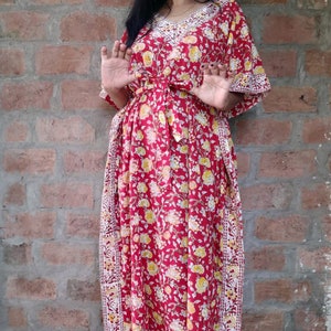May include: A red floral maxi dress with a white trim and a tie at the waist. The dress has a V-neck and 3/4 sleeves.