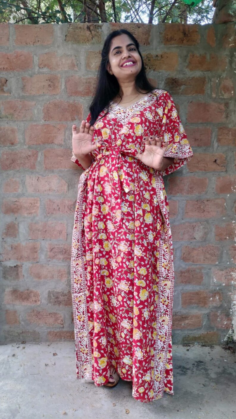 May include: A red floral maxi dress with a white trim and a tie at the waist. The dress has a V-neck and 3/4 sleeves.