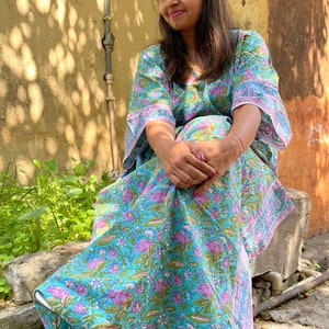 May include: A woman wearing a blue and pink floral print kaftan with long sleeves and a V-neck. The kaftan is made of cotton and has a relaxed fit.