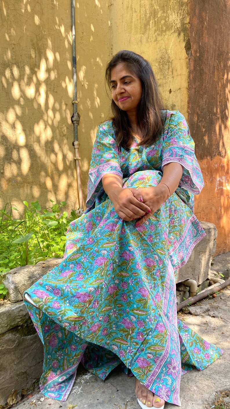 May include: A woman wearing a blue and pink floral print kaftan with long sleeves and a V-neck. The kaftan is made of cotton and has a relaxed fit.