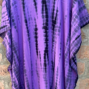 Puede incluir: Una kaft&aacute;n larga de color morado y negro con estampado tie-dye, cuello en V y mangas cortas.