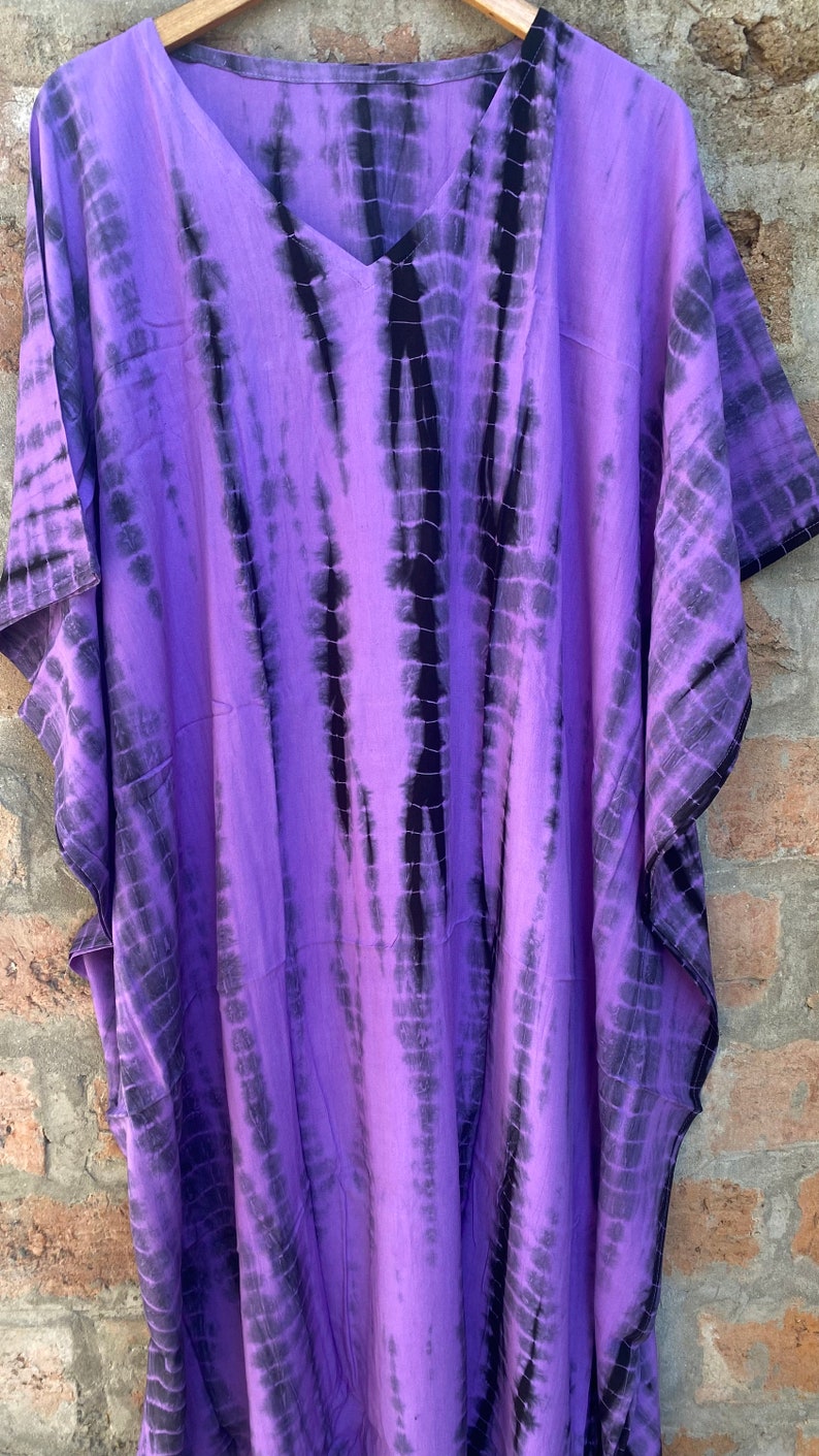 Puede incluir: Una kaft&aacute;n larga de color morado y negro con estampado tie-dye, cuello en V y mangas cortas.