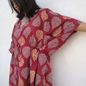 May include: A maroon kaftan with a silver and gold leaf print. The kaftan has a drawstring waist and long sleeves.