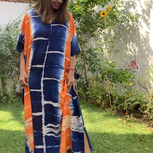 May include: A long, flowing, orange and blue tie-dye kaftan with a V-neckline. The kaftan has a side slit and is made of a soft, comfortable fabric.