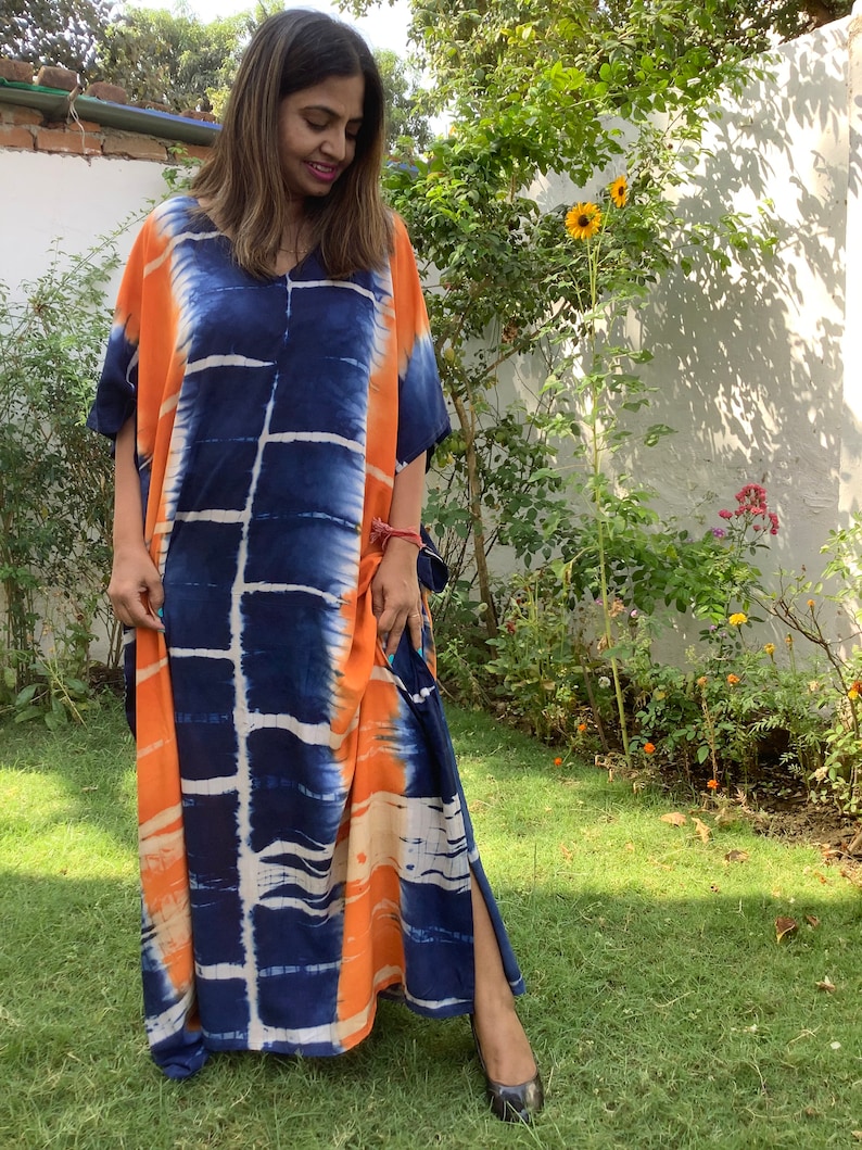 May include: A long, flowing, orange and blue tie-dye kaftan with a V-neckline. The kaftan has a side slit and is made of a soft, comfortable fabric.