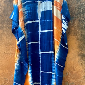 May include: A long, blue and orange tie-dye kaftan with a V-neckline. The kaftan has a loose, flowing fit and is perfect for a casual, summery look.