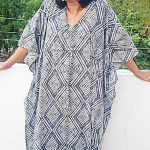 May include: A white and black geometric print kaftan with a V-neckline and long sleeves. The kaftan is made of a lightweight fabric and has a relaxed fit.