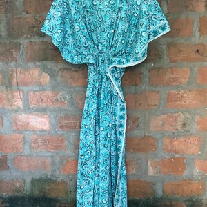 May include: A turquoise blue kaftan with a white floral print. The kaftan has a V-neck and short sleeves. It is made of a lightweight fabric and has a tie at the waist.