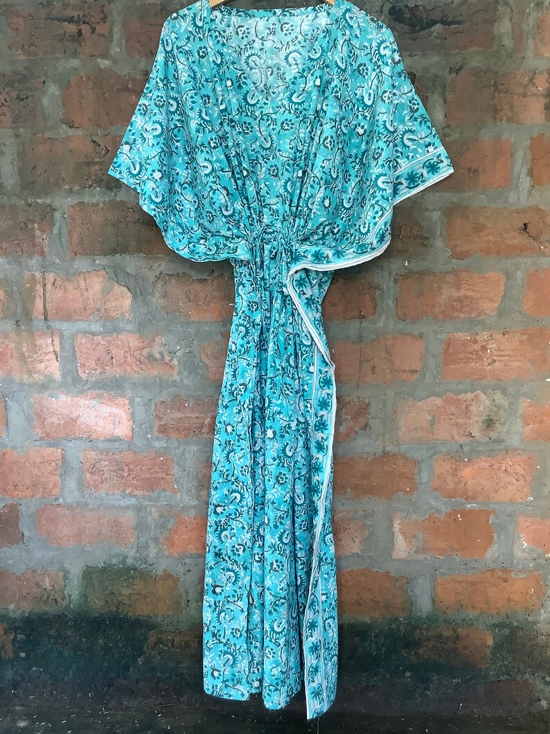 May include: A turquoise blue kaftan with a white floral print. The kaftan has a V-neck and short sleeves. It is made of a lightweight fabric and has a tie at the waist.