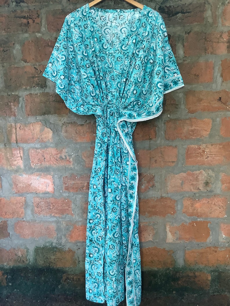May include: A teal blue kaftan with a white floral print. The kaftan has a V-neck and short sleeves. It is made of a lightweight fabric and has a tie at the waist.