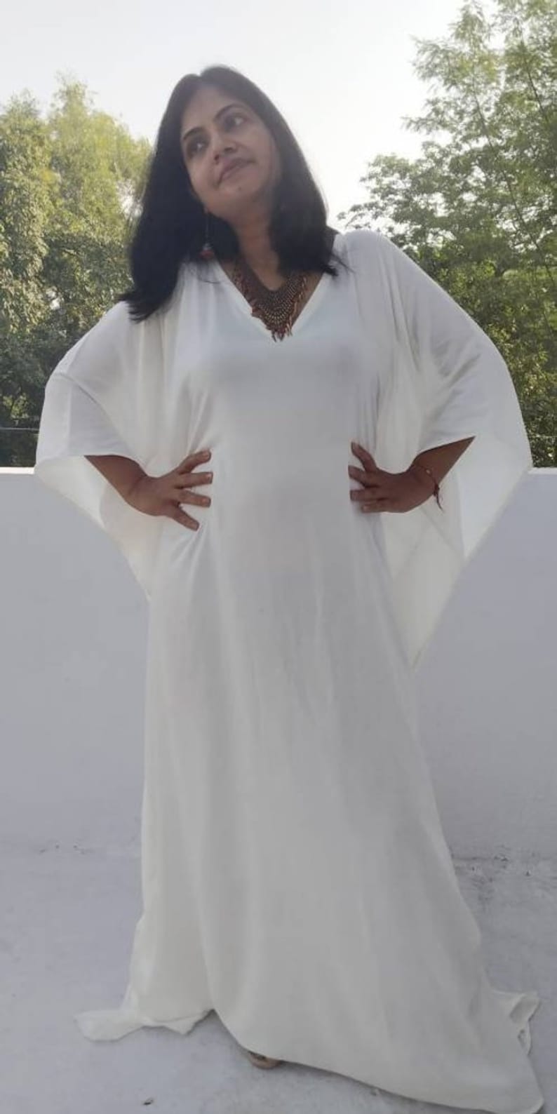 May include: A white maxi dress with long, flowing sleeves and a V-neckline. The dress is made of a lightweight fabric and has a relaxed fit.