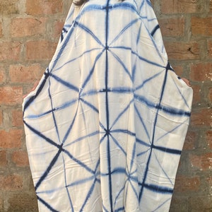 May include: A white caftan dress with a geometric blue pattern. The dress has a V-neck and wide sleeves. The fabric appears to be lightweight and flowing, suitable for warm weather. The dress is worn by a person.