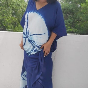 Op de afbeelding: Een vrouw draagt een blauwe en witte tie-dye maxi-jurk met een witte en blauwe wedge-hak.