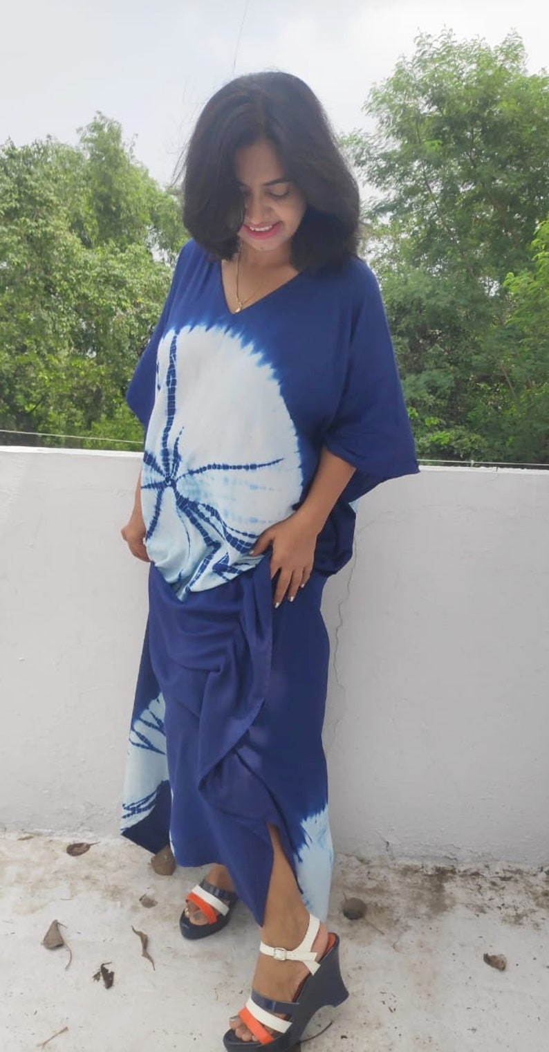 Op de afbeelding: Een vrouw draagt een blauwe en witte tie-dye maxi-jurk met een witte en blauwe wedge-hak.