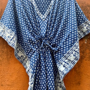 May include: A blue and white cotton kaftan with a floral print. The kaftan has a V-neck and a tie at the waist.