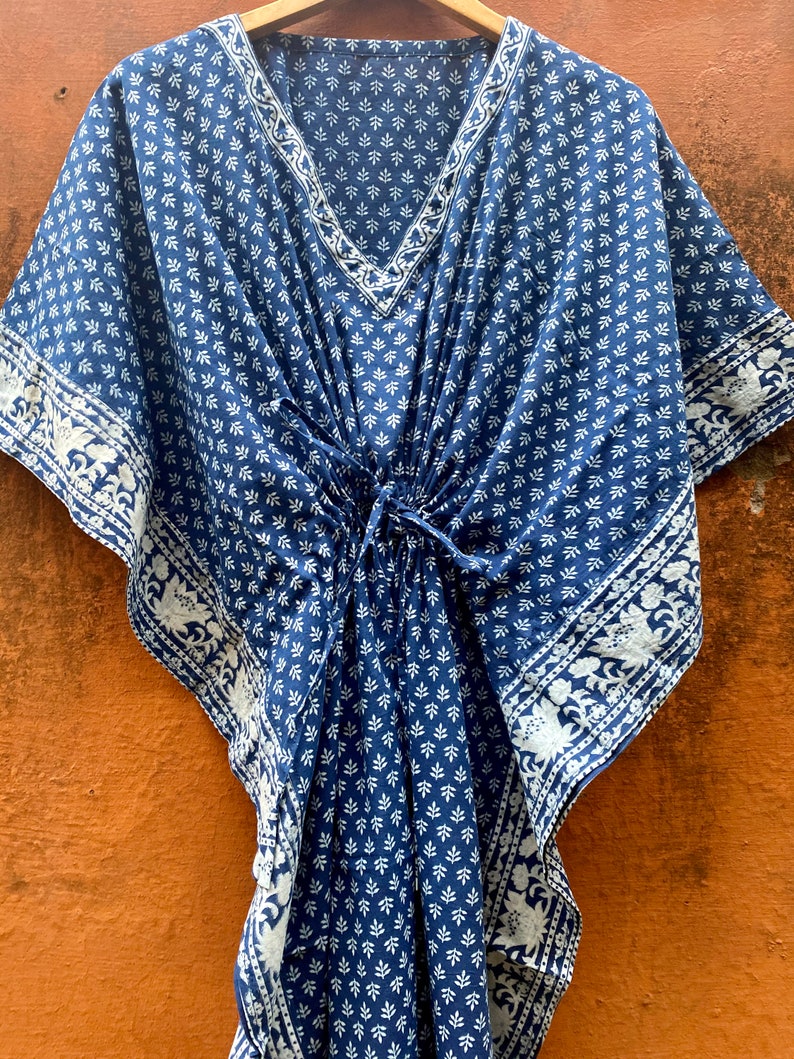 May include: A blue and white cotton kaftan with a floral print. The kaftan has a V-neck and a tie at the waist.