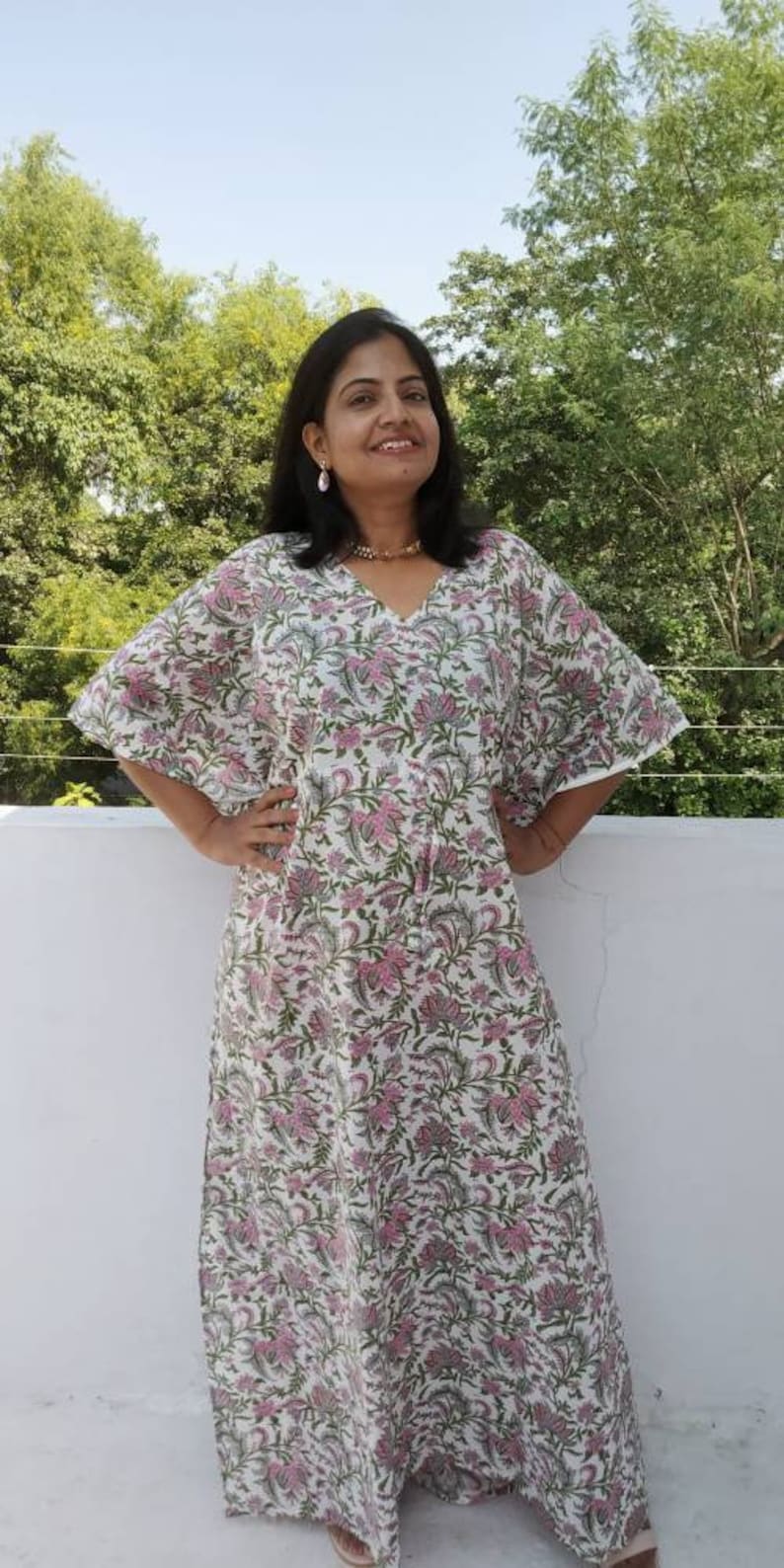 May include: A white maxi dress with a pink and green floral print. The dress has a V-neck and a flowing silhouette.