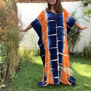 May include: A long, flowing, orange and blue tie-dye kaftan dress with a V-neckline. The dress is made of a soft, lightweight fabric and has a relaxed fit.
