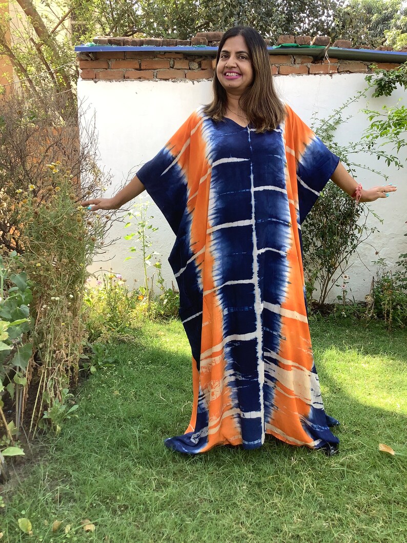 May include: A long, flowing, orange and blue tie-dye kaftan dress with a V-neckline. The dress is made of a soft, lightweight fabric and has a relaxed fit.