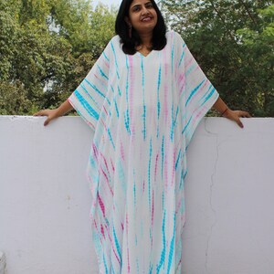 May include: A white, blue, and pink tie-dye kaftan with a V-neckline. The kaftan is loose-fitting and has long sleeves.