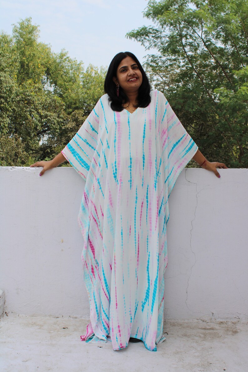 May include: A white, blue, and pink tie-dye kaftan with a V-neckline. The kaftan is loose-fitting and has long sleeves.