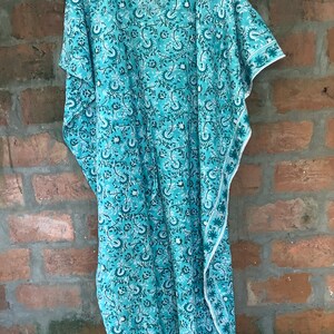 May include: A turquoise blue kaftan with a white floral print. The kaftan has a V-neck and short sleeves. The fabric is lightweight and flowy.