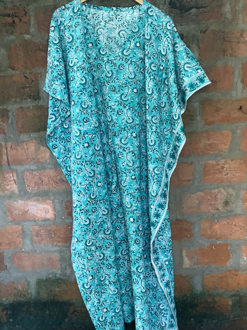 May include: A turquoise blue kaftan with a white floral print. The kaftan has a V-neck and short sleeves. The fabric is lightweight and flowy.