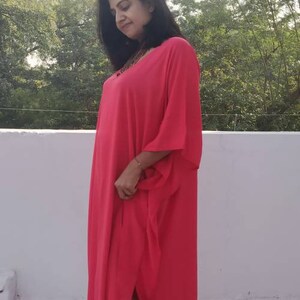May include: A woman wearing a long, bright pink maxi dress with a side slit. The dress has a loose, flowing fit and is made of a lightweight fabric. She is wearing white wedge sandals.