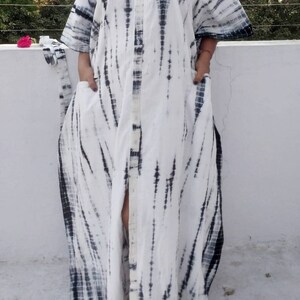 Puede incluir: Un vestido maxi blanco con un estampado tie-dye negro. El vestido tiene un frente abotonado y una abertura lateral.
