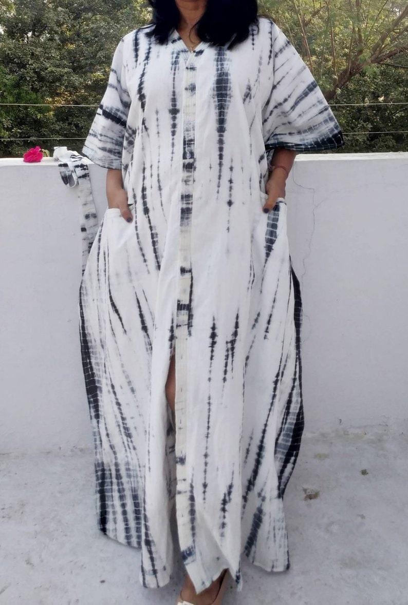 Puede incluir: Un vestido maxi blanco con un estampado tie-dye negro. El vestido tiene un frente abotonado y una abertura lateral.