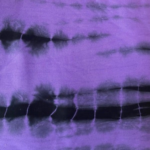 Puede incluir: Tela de tie-dye morado y negro con un patr&oacute;n horizontal. La tela tiene un tacto suave y texturizado.