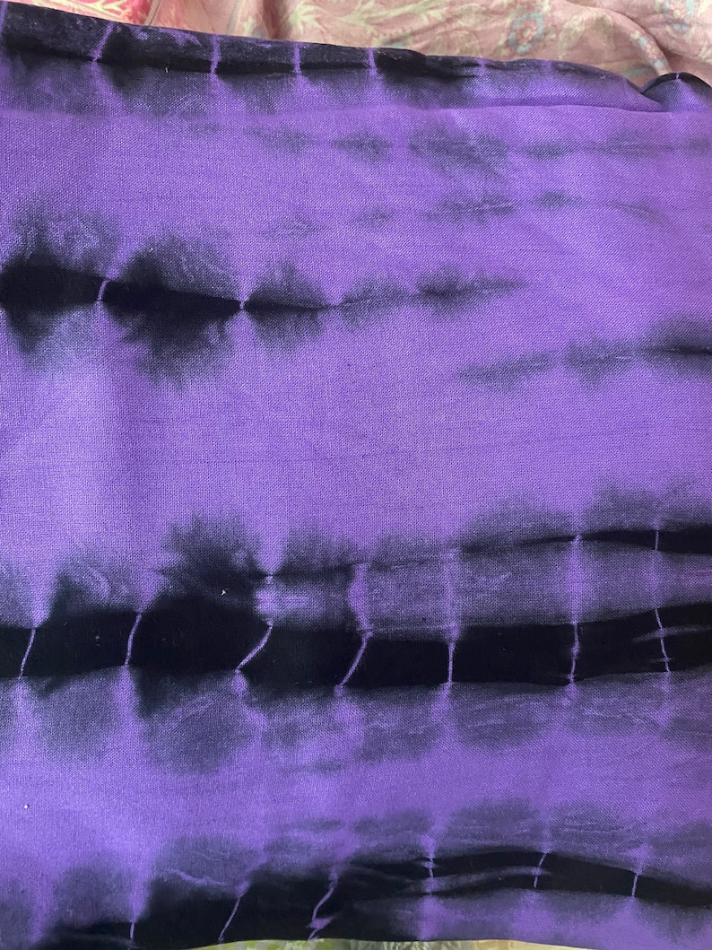 Puede incluir: Tela de tie-dye morado y negro con un patr&oacute;n horizontal. La tela tiene un tacto suave y texturizado.