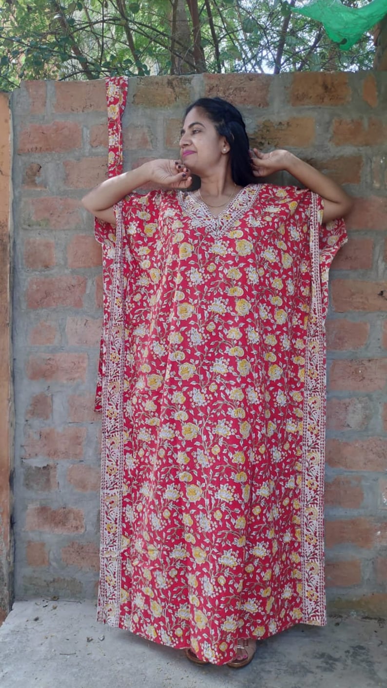 May include: A red and white floral print kaftan with a white trim. The kaftan has a V-neck and short sleeves.