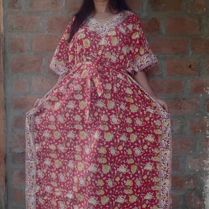 May include: A red floral print kaftan with white trim. The kaftan has a V-neckline and a tie at the waist.