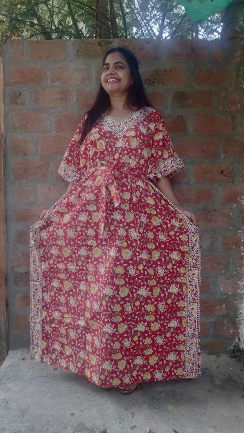 May include: A red floral print kaftan with white trim. The kaftan has a V-neckline and a tie at the waist.