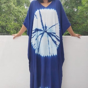 Op de afbeelding: Een lange, vloeiende blauwe en witte tie-dye kaftan met een groot cirkelvormig patroon. De kaftan heeft een V-hals en korte mouwen.