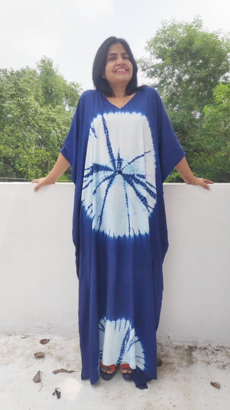 Op de afbeelding: Een lange, vloeiende blauwe en witte tie-dye kaftan met een groot cirkelvormig patroon. De kaftan heeft een V-hals en korte mouwen.