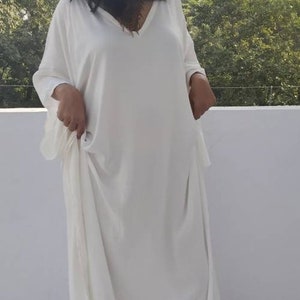 May include: A white, long-sleeved, loose-fitting kaftan dress with a V-neckline.