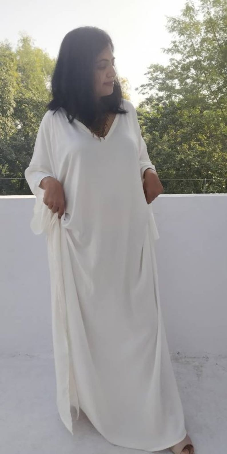 May include: A white, long-sleeved, loose-fitting kaftan dress with a V-neckline.
