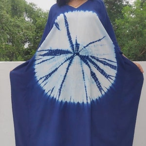 Op de afbeelding: Een lange, vloeiende blauwe en witte tie-dye kaftanjurk met een cirkelvormig patroon. De jurk heeft een V-hals en is gemaakt van een zachte, comfortabele stof.