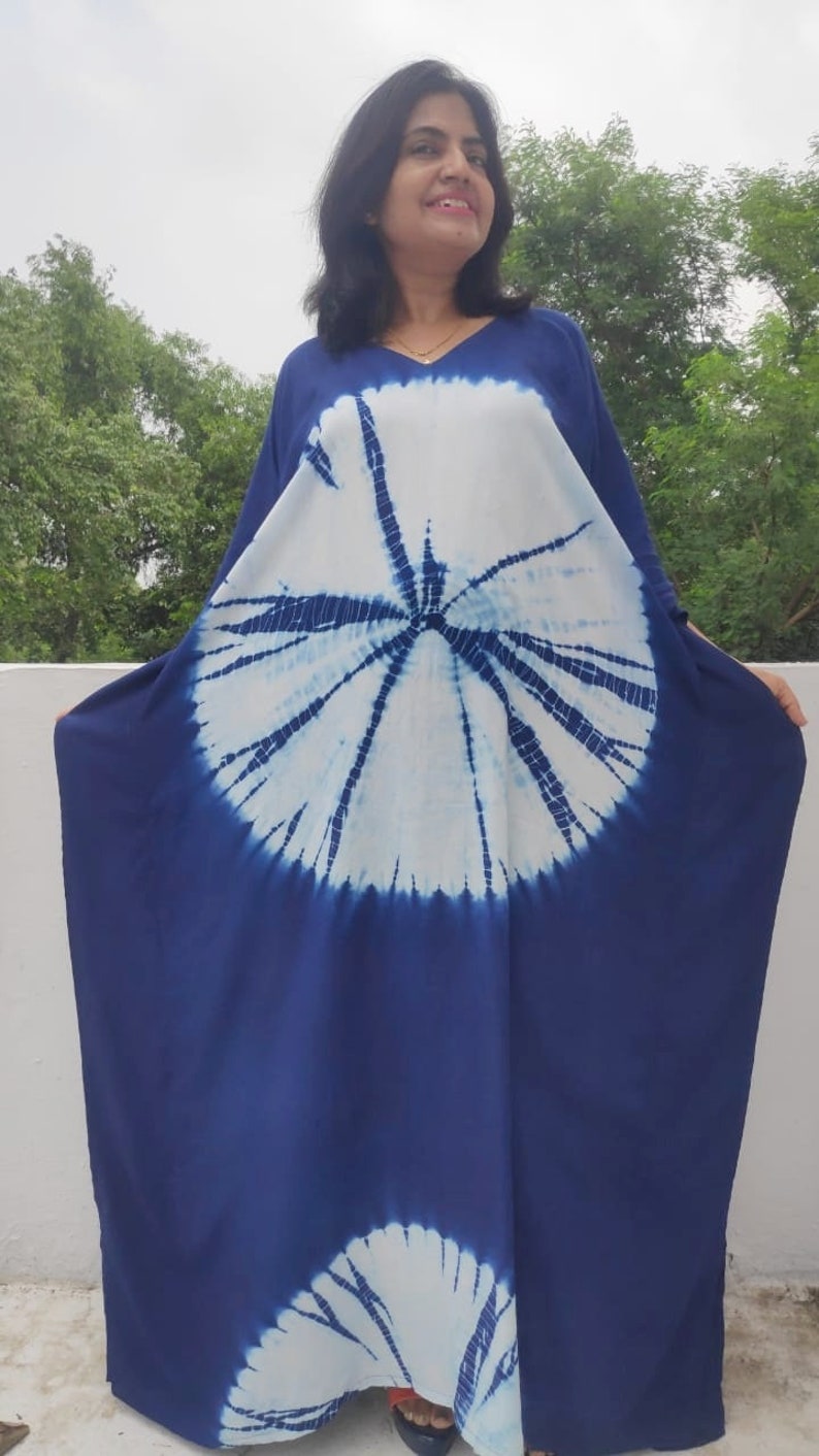 Op de afbeelding: Een lange, vloeiende blauwe en witte tie-dye kaftanjurk met een cirkelvormig patroon. De jurk heeft een V-hals en is gemaakt van een zachte, comfortabele stof.