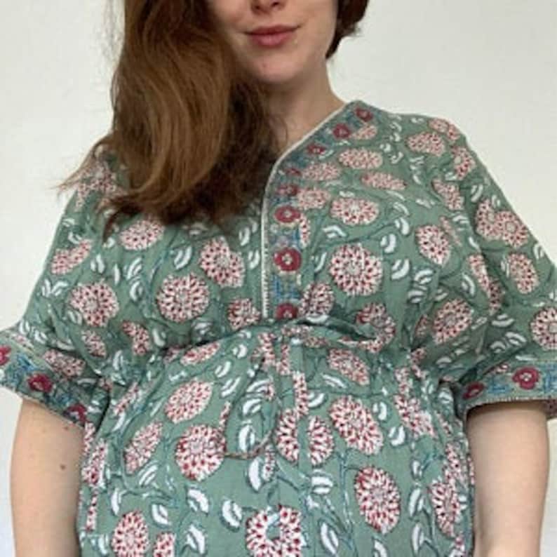 May include: A green kaftan with a floral print, featuring a V-neckline and short sleeves. The kaftan has a cinched waist and a flowing skirt.