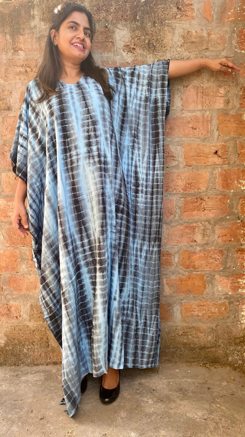 May include: A blue and black tie-dye kaftan dress with a loose, flowing silhouette. The dress has a round neckline and long sleeves.