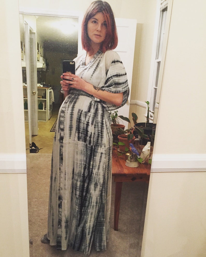 Puede incluir: Una mujer con un vestido largo de maxi de tie-dye blanco y negro. Est&aacute; de pie frente a un espejo y sostiene un tel&eacute;fono m&oacute;vil en la mano.