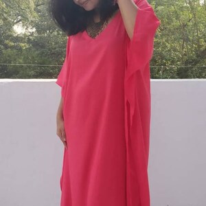 May include: A bright pink kaftan with a V-neckline and long sleeves. The kaftan is made of a lightweight fabric and has a flowing silhouette.