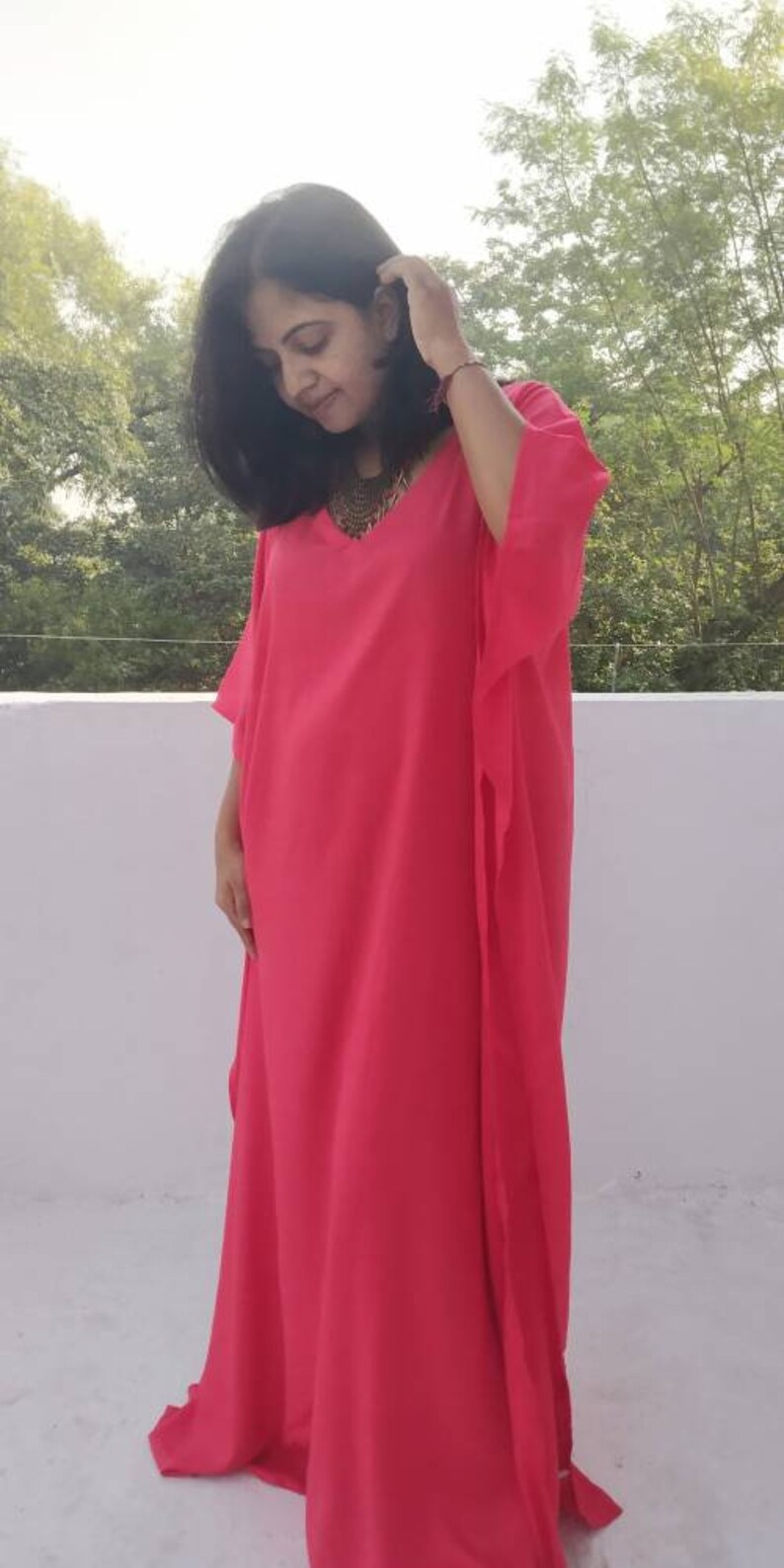 May include: A bright pink kaftan with a V-neckline and long sleeves. The kaftan is made of a lightweight fabric and has a flowing silhouette.
