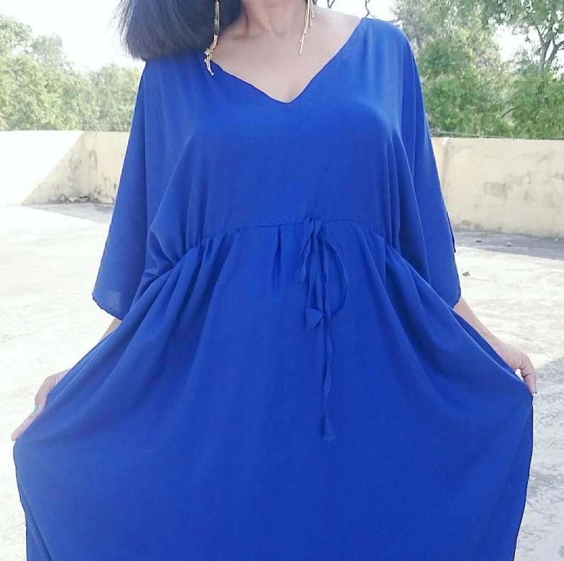 May include: A vibrant blue dress with a V-neckline and flowing sleeves. The dress features a cinched waist with a drawstring detail. The fabric appears lightweight and drapes elegantly. The overall style is relaxed and comfortable.